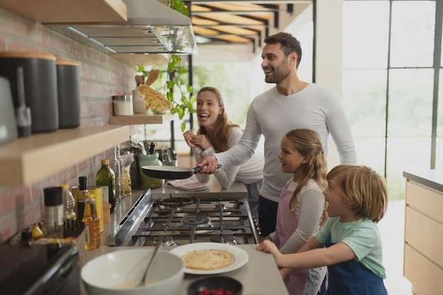 Front view of a family cooking together under a range hood Front view of a family cooking together under a range hood