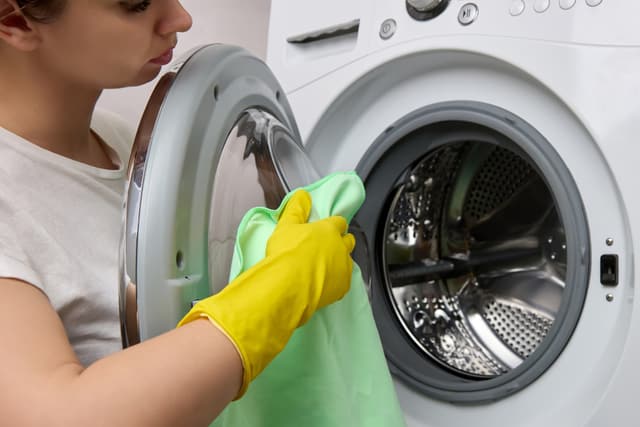 Front view of a woman cleaning her washing machine Front view of a woman cleaning her washing machine