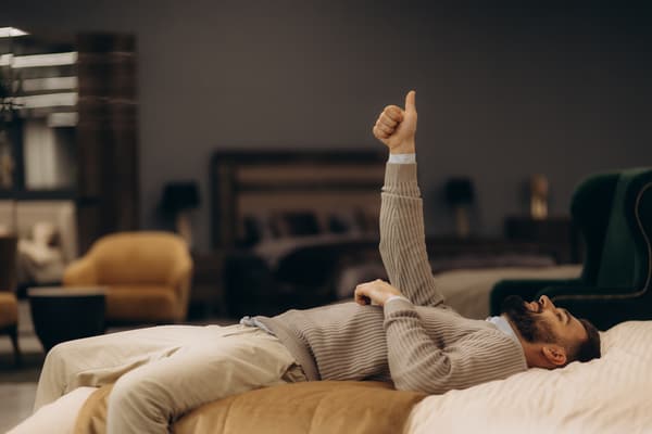 A man lying on a bed giving a thumb up.