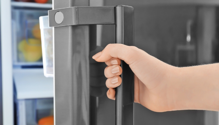 Close-up of a hand opening a stainless steel refrigerator door by its handle