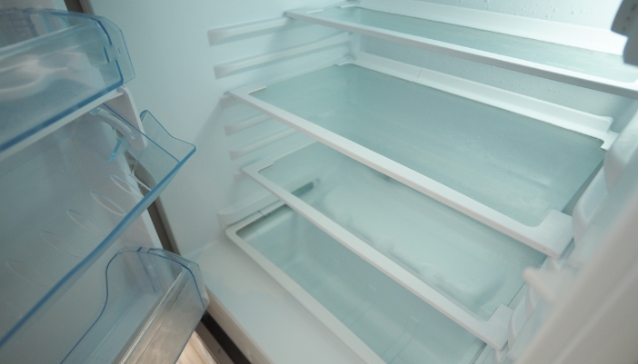 Open refrigerator door revealing empty glass shelves and door bins inside